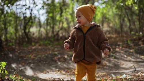 Lovely Caucasian baby runs in the park. Smiling toddler in cap and jacket walking in autumn nature.