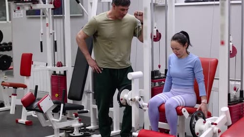 A Middleaged Woman During Gym Workout Leg Extensions Under the Supervision of a Trainer