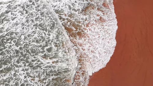 Huge sea waves with white foam breaking on golden sandy beach