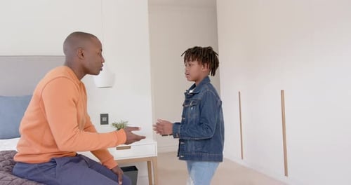 Happy african american father and son talking and embracing at home, slow motion