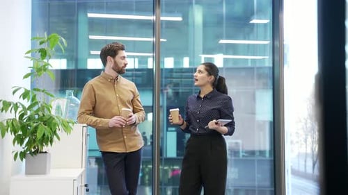 Two colleagues engaged in friendly conversation with coffee in modern office setting. Co-workers,