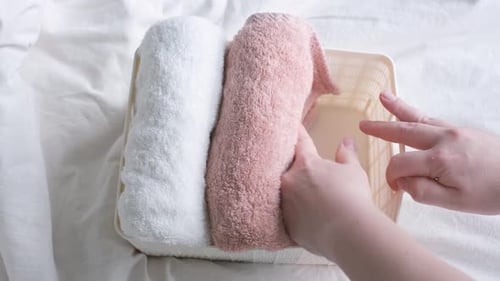 Female hands folding towels in plastic box on the background of a white bedspread, top view.