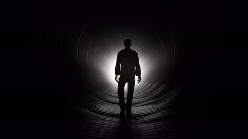 Silhouette of Man Walking Towards Light in Dark Tunnel