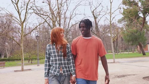 Young Interracial Couple Holding Hands and Walking in Park
