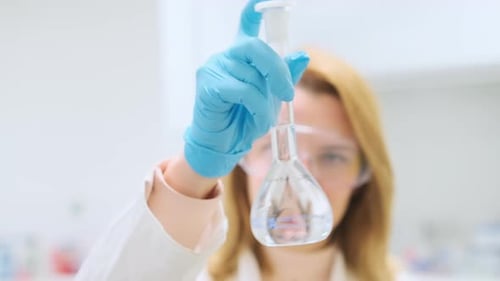 Focused Scientist in Goggles Shakes Glass Flask with Water