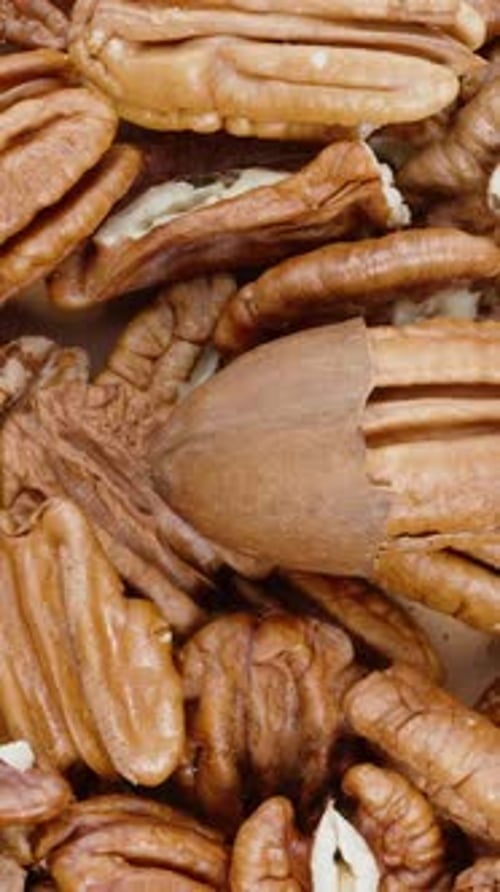 Vertical video. Top view of a table covered with both peeled and unshelled pecans.