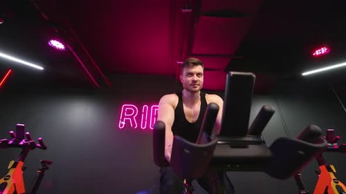 Speedy bicycle ride in fitness centre. Fitness man athlete training using exercise bike in gym