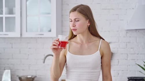 Young Woman Drinks Red Juice in Bright Kitchen