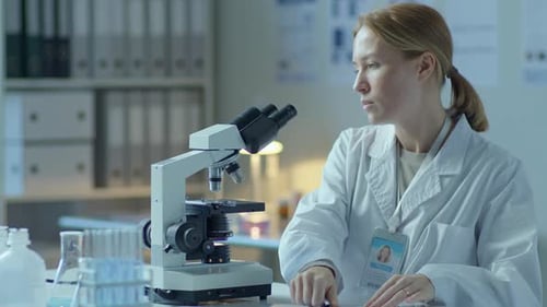 Focused Woman Analyzing Sample Under Microscope in Lab