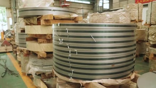 Large steel strip coils are stacked and stored inside an industrial metal processing factory