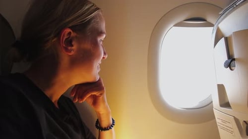 Woman Looks Out Airplane Window During Flight