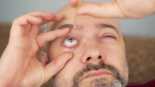 Man Applying Eye Drops in Dry Irritated Eyes Sitting on Sofa at Home Person Using Eyedrops