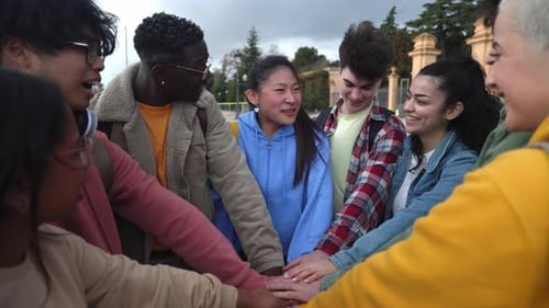 Young Group of Friends Stacking Hands Together and Celebrating Outdoors