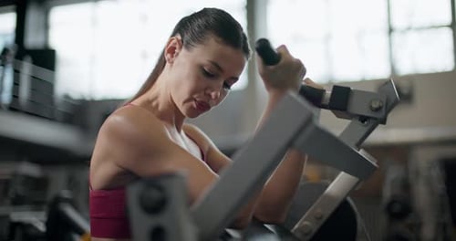 A Young Beautiful Girl in Sportswear Exercises on a Machine in the Gym Doing Exercises for Her Arms