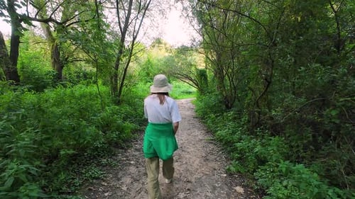 A young girl walks along a forest path among trees and grass in a summer forest.