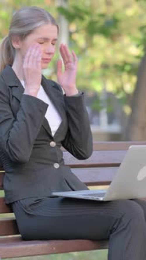Woman works on laptop with headache in park