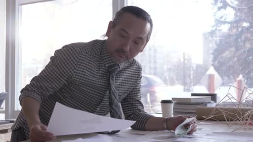 Man Inspecting Blueprints at a Bright Office Workspace
