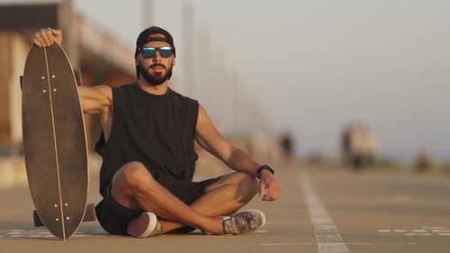 Adult Attractive Man Hipster Sitting on the Road Holding a Longboard