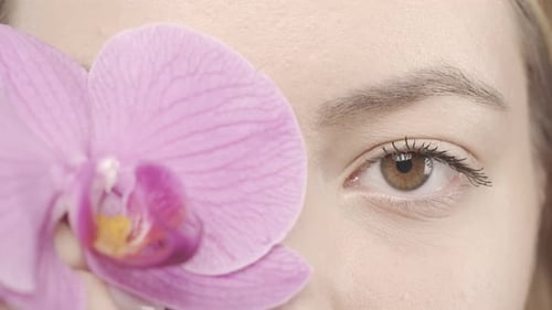 Beautiful Eyes of a Young Woman Close Up A Woman Covers Her Eye with an Orchid Flower Good Vision
