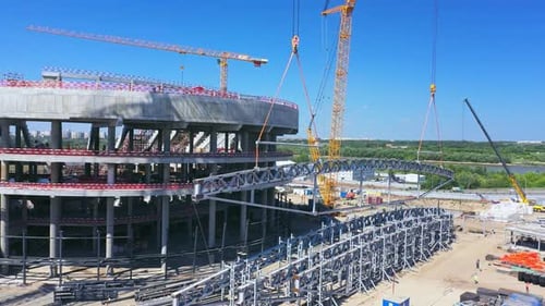 Una parte de la carcasa de acero cuelga de grúas y polipastos en un estadio deportivo