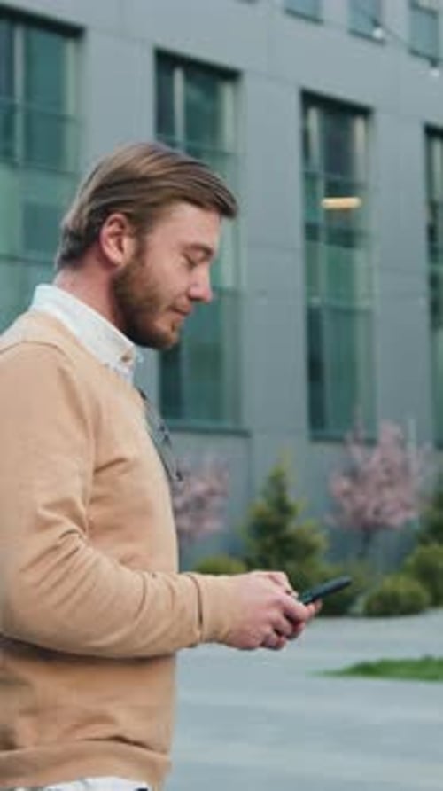 Side View Tracking Shot of Young Handsome Young Businessman Text Messaging on Cell Phone While
