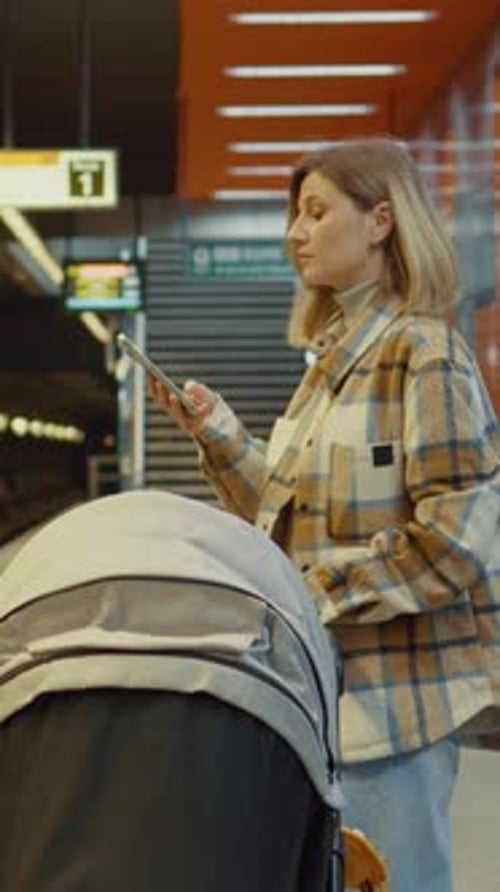 Vertical Screen Mother waiting for subway using phone while holding stroller