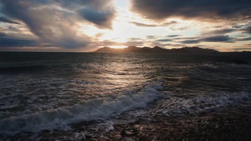 Evening waves washing over a rocky shoreline under dramatic clouds and warm sunset light