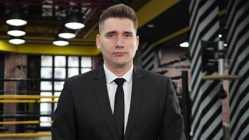 Businessman in a Suit Standing in Boxing Gloves on the Background of the Ring
