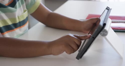 Child's left finger is starting tapping, right hand is steadying tablet on white table for study