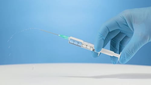 Medical gloves hand injecting vaccination liquid with syringe, blue background