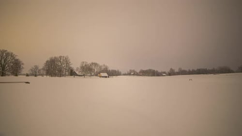 Static night scene time-lapse of snowy white countryside field with house and clearing cloudy sky ba