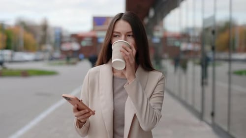Stylish Young Business Woman Using Smartphone Walking on the Street During Her Coffee Break