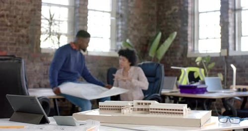 Diverse architect colleagues discussing work with building model and blueprint in slow motion