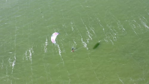 Aerial top-down shot of a kitesurfer riding on the kite on the strong wind and short waves