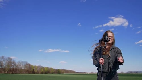 Woman Singing into Microphone in Open Field