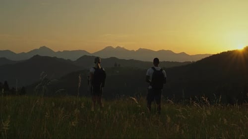 Couple admiring a scenic mountain sunset before continuing their peaceful evening hike