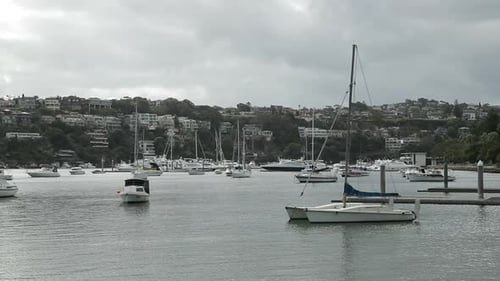 Sailboats moored in bay of seaside town on cloudy day, medium shot
