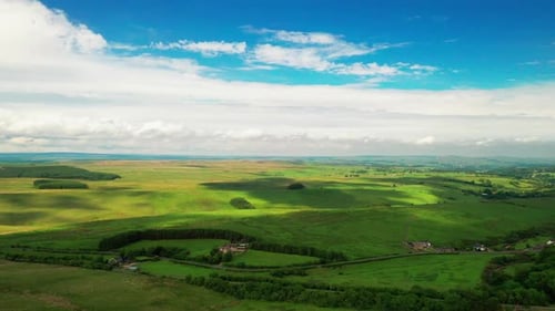 Aerial landscape shot showing lush green farmland, on a bright blue sky day.