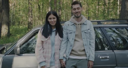 Slow Motion Portrait of Happy Couple Students Standing Next to Modern Car Smiling Outdoors in Forest