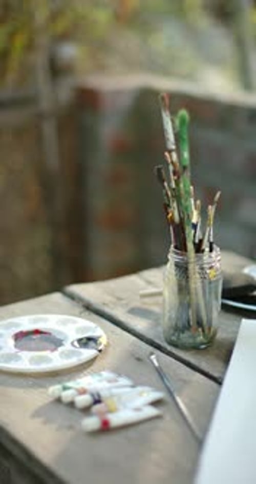 Vertical video: Camera pulling focus toward jar of brushes on wooden table revealing brush tips