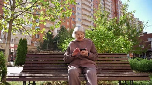 Senior Woman Uses Smartphone on Park Bench