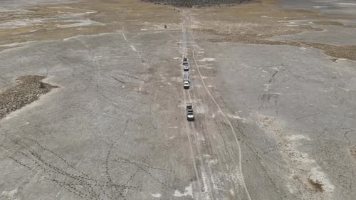 Convoy of off-road trucks drives across rugged, barren plains, aerial