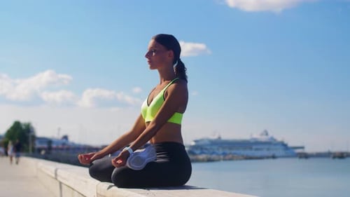 Woman Meditating by Water on Bright Sunny Day