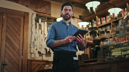 Front View of Man in Black Apron Using Tablet While Standing Near Bar Counter