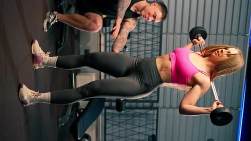 Woman Doing Barbell Squats with Trainer in Gym