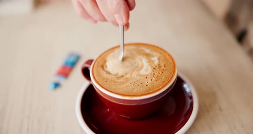 Hand stirs creamy coffee in a brown cup