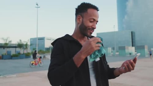 Young athlete dressed in hoodie uses cellphone after training while standing on the embankment