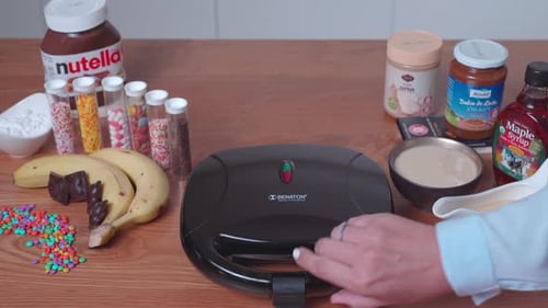 Frau öffnet Waffeleisen beim Zubereiten von Waffeln in der Küche