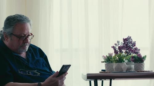 Senior Man Uses Smartphone at Home During Day