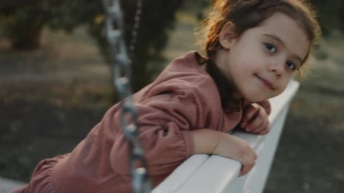 Little 5 Yo Girl Having Fun on a White Swing in a Quiet Treelined Park Background Preschooler
